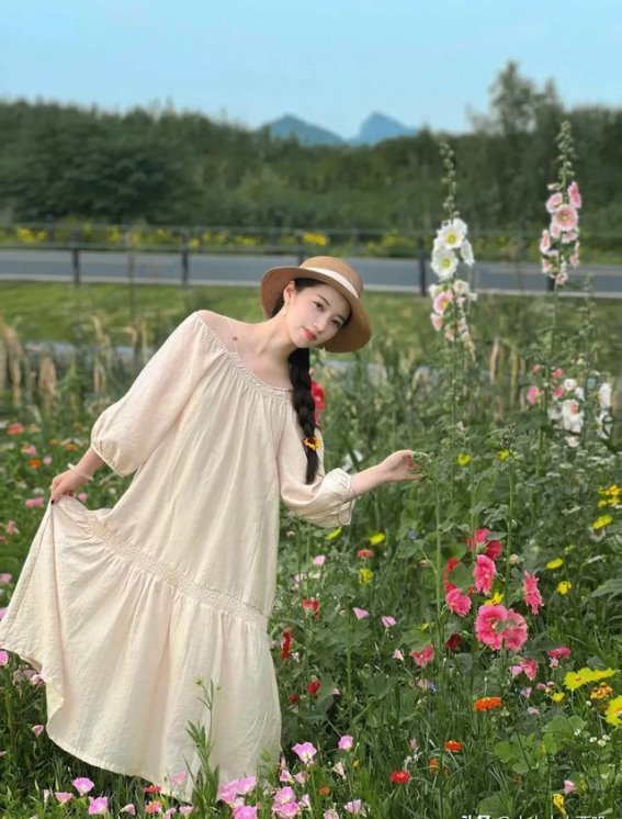 《花海中的静谧与神奇：米黄色长裙女子的自然之旅》在一个温暖的午后，一位穿着米黄色长裙的年轻女子，如同花海中的仙子般，与自然和谐共处。她站立在阳光斜射的路边花丛中，裙摆随风轻轻飘动，仿佛时间在这一刻停止流动。她不仅是花海的守护者，更是大自然与人类和谐共生的完美诠释。